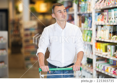 Male shopper with trolley in trading floor browses eco product in bio shop search perfect goods Male shopper with trolley in trading floor browses eco product in bio shop search perfect goods 115303735
