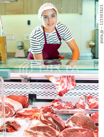 Young female butcher putting raw meat on supermarket display 115303823