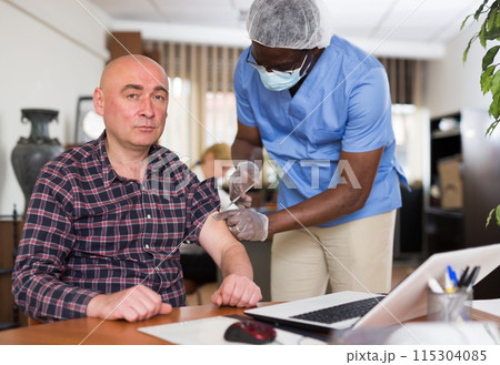 Entrepreneur getting vaccinated by african american doctor in office 115304085