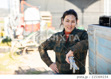 Positive Asian workwoman standing in backyard of farm on spring day 115304154