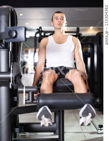 Sportive young guy training on leg extension machine in gym 115304362
