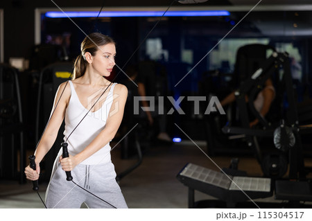 Active athlete young woman during exercises on crossover exercise machine with loops and weighting Active athlete young woman during exercises on crossover exercise machine with loops and weighting 115304517