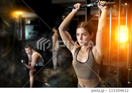 Slender athletic girl work out muscles of arms and shoulders on simulator in gym of fitness club 115304612