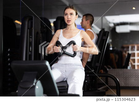 Sportive young girl training her arms using cable exercise machine in gym 115304623