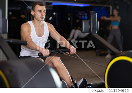 Sportive young guy training on cable row machine in gym Sportive young guy training on cable row machine in gym 115304696