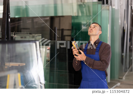 Male worker using control panel and lifting mechanism controls movement of window panes in an industrial workshop Male worker using control panel and lifting mechanism controls movement of window panes in an industrial workshop 115304872