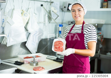 Female butcher demonstrating freshly formed beef hamburger patties 115305004
