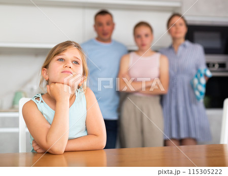 Sad preschooler girl sits at table while parents and older sister scold Sad preschooler girl sits at table while parents and older sister scold 115305222
