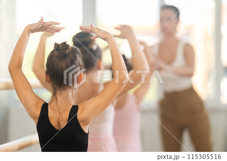 Girls in ballet class perform fifth position with correction of female mentor 115305516