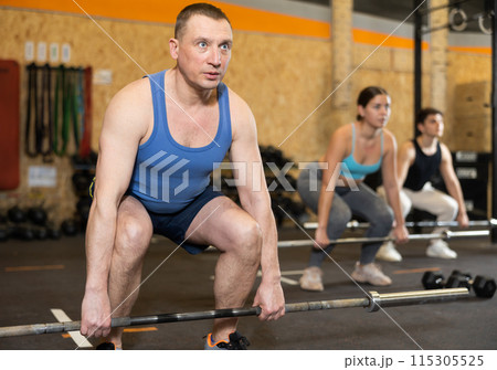 Man exercising with barbell during intense group workout Man exercising with barbell during intense group workout 115305525