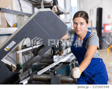 Glass workshop - girl works on machine for cutting aluminum profiles for windows 115305540