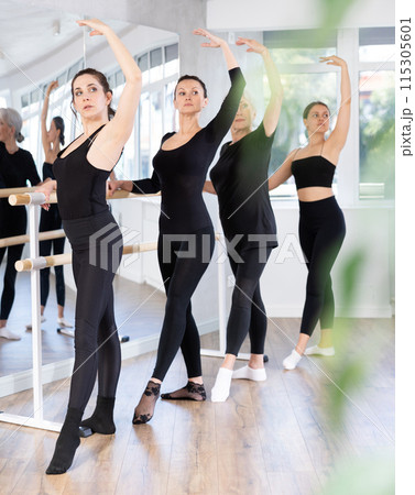 Female ballet trainer teaching group of dancers near ballet barre in dancing studio Female ballet trainer teaching group of dancers near ballet barre in dancing studio 115305601