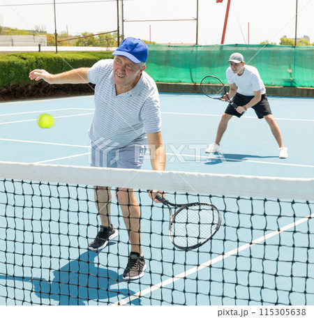 Man with black racket playing match in open behind net court outdoors. Man with black racket playing match in open behind net court outdoors. 115305638
