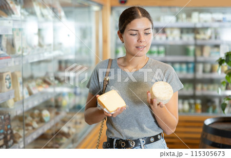 Girl in bio food store holds cheese of different varieties in hands and is thinking about buying Girl in bio food store holds cheese of different varieties in hands and is thinking about buying 115305673