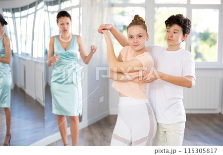 Experienced dance teacher teaching ballroom dancing to a couple of teenagers in studio Experienced dance teacher teaching ballroom dancing to a couple of teenagers in studio 115305817