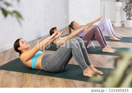 Sporty fit young women pumping abs and back on mats while training together in comfortable fitness center 115305835