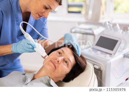 Mature woman undergoing hardware cosmetic facial treatment using ultrasonic shovel Mature woman undergoing hardware cosmetic facial treatment using ultrasonic shovel 115305976