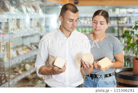 Positive young couple choosing cheese in large supermarket Positive young couple choosing cheese in large supermarket 115306291