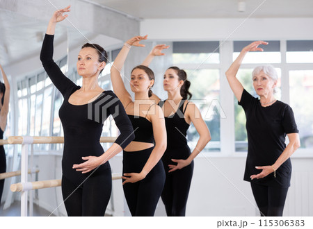 Mature teacher conducts class with girls in ballet studio, observes doing forth position exercise. Mature teacher conducts class with girls in ballet studio, observes doing forth position exercise. 115306383