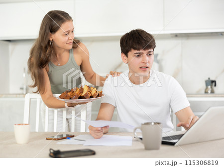 Young woman offering pie to guy working at laptop 115306819