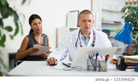 Doctor writing prescription to female patient on laptop at clinic Doctor writing prescription to female patient on laptop at clinic 115306829
