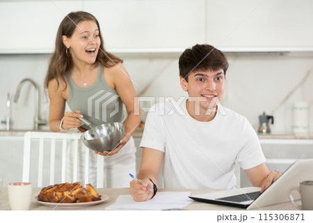 Happy young man using laptop in the kitchen while communicating with his girlfriend 115306871