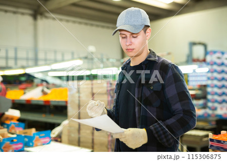 Positive male worker fills out a document at a citrus processing plant. 115306875
