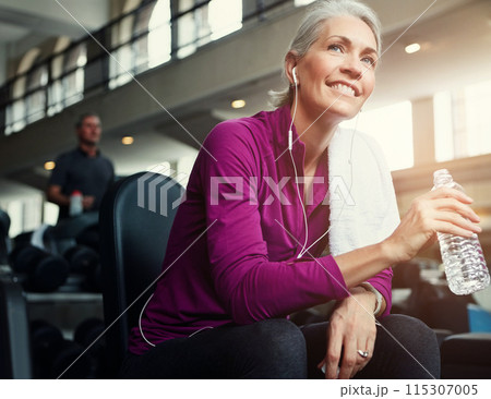 Fitness, relax and senior woman in gym with water bottle for training, exercise and workout. Sports, retirement and person listening to music, resting and drinking for wellness, health and hydration 115307005