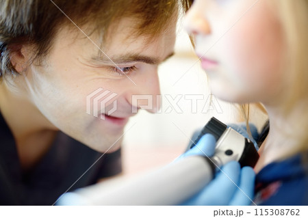 A caring doctor checks moles on the skin of a small child. A dermatologist looks at a rash on the chest of a girl using a dermatoscope. A caring doctor checks moles on the skin of a small child. A dermatologist looks at a rash on the chest of a girl using a dermatoscope. 115308762