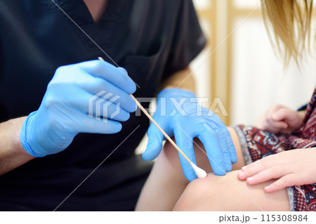 A caring doctor checks moles on the skin of a small child. Dermatologist remove of benign tumors with liquid nitrogen for cute preschooler girl. Baby fears of treat. 115308984