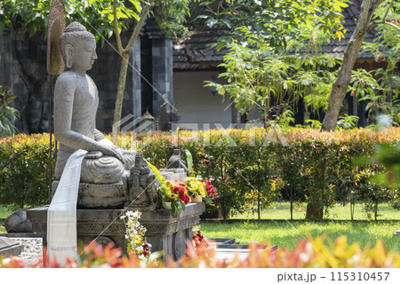 Stone statue of Buddha sitting on a stone pedestal surrounded by trees Stone statue of Buddha sitting on a stone pedestal surrounded by trees 115310457