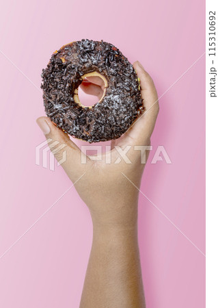 A human hand holding a delicious donut with a chocolate sprinkle decoration A human hand holding a delicious donut with a chocolate sprinkle decoration 115310692
