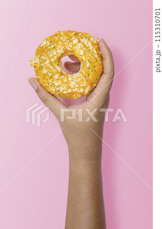 Hand holding a sprinkled donut on pink background 115310701