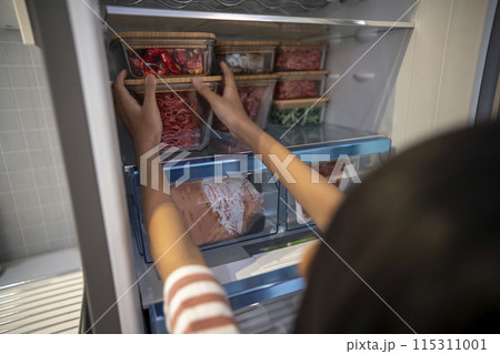 A little girl arranges a snack container on the refrigerator 115311001