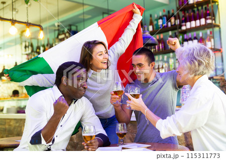 Extremely happy italian man and woman supporters waving national flag, celebrating victory with glasses of beer in pub Extremely happy italian man and woman supporters waving national flag, celebrating victory with glasses of beer in pub 115311773