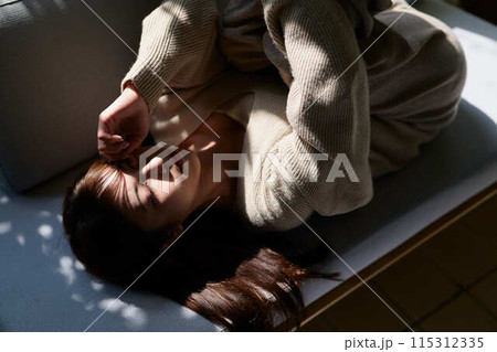 窓辺で日差しを浴びながら寝る女性 115312335
