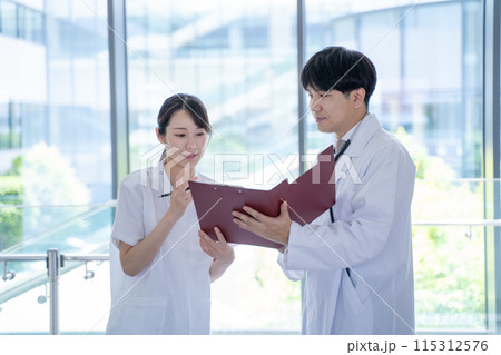 病院でカルテを見ながら相談する男性医師と看護師 病院でカルテを見ながら相談する男性医師と看護師 115312576