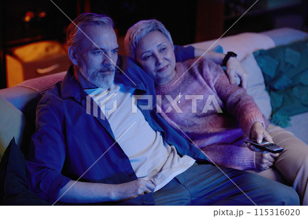 Portrait of senior couple watching movie together sitting on couch at home in blue light copy space Portrait of senior couple watching movie together sitting on couch at home in blue light copy space 115316020