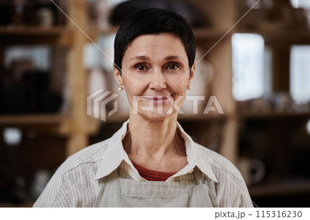 Portrait of adult Caucasian woman wearing apron and looking at camera wearing apron in pottery studio, copy space 115316230