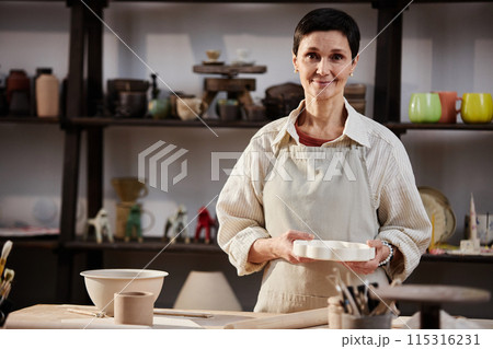 Waist up portrait of mature Caucasian woman as female artisan smiling at camera in pottery studio, copy space Waist up portrait of mature Caucasian woman as female artisan smiling at camera in pottery studio, copy space 115316231