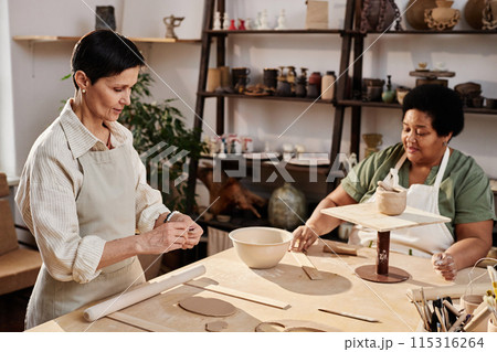 High angle view at two senior women enjoying pottery class in art studio lit by sunlight copy space High angle view at two senior women enjoying pottery class in art studio lit by sunlight copy space 115316264