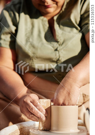 Vertical closeup of senior African American woman enjoying pottery class in sunlight 115316353