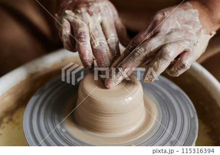 Close up of hands carefully shaping clay on pottery wheel creating unique ceramics copy space 115316394