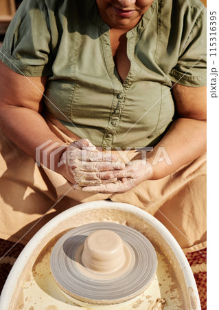 Vertical closeup of senior African American woman enjoying pottery class in sunlight and shaping clay Vertical closeup of senior African American woman enjoying pottery class in sunlight and shaping clay 115316395