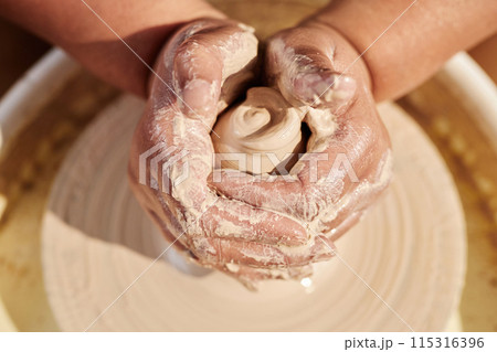 Close up of female hands shaping clay on pottery wheel and creating handmade ceramics in sunlight copy space 115316396