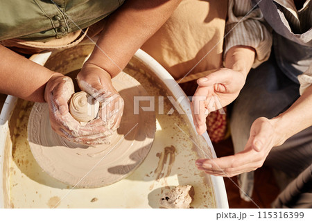 Top view closeup of two women creating ceramics together at pottery wheel lit by sunlight copy space 115316399