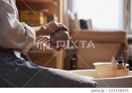 Side view closeup of unrecognizable adult woman gently holding clay ball in hands and enjoying ceramics class copy space 115316425