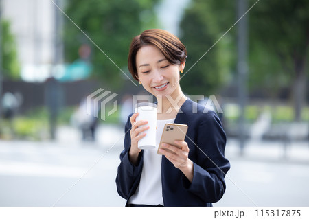 ビジネス　スマホを見ながら飲み物を飲んでいる女性 115317875