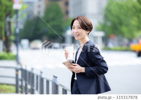 ビジネス　スマホを見ながら飲み物を飲んでいる女性 115317878