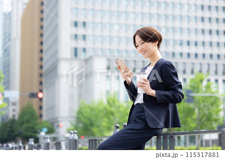 ビジネス　スマホを見ながら飲み物を飲んでいる女性 115317881